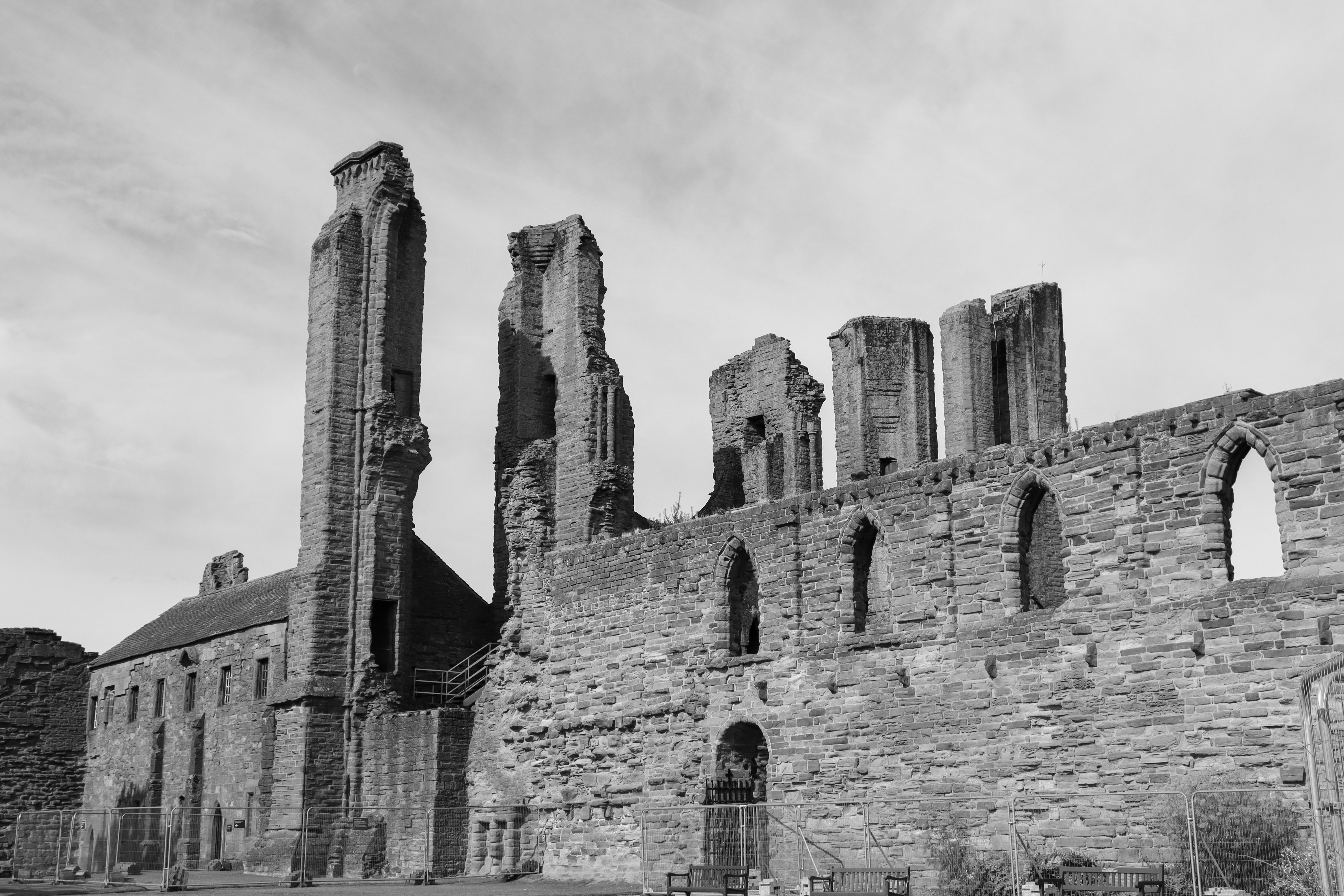 Black and white photo of stone ruins with five towers rising behind a wall