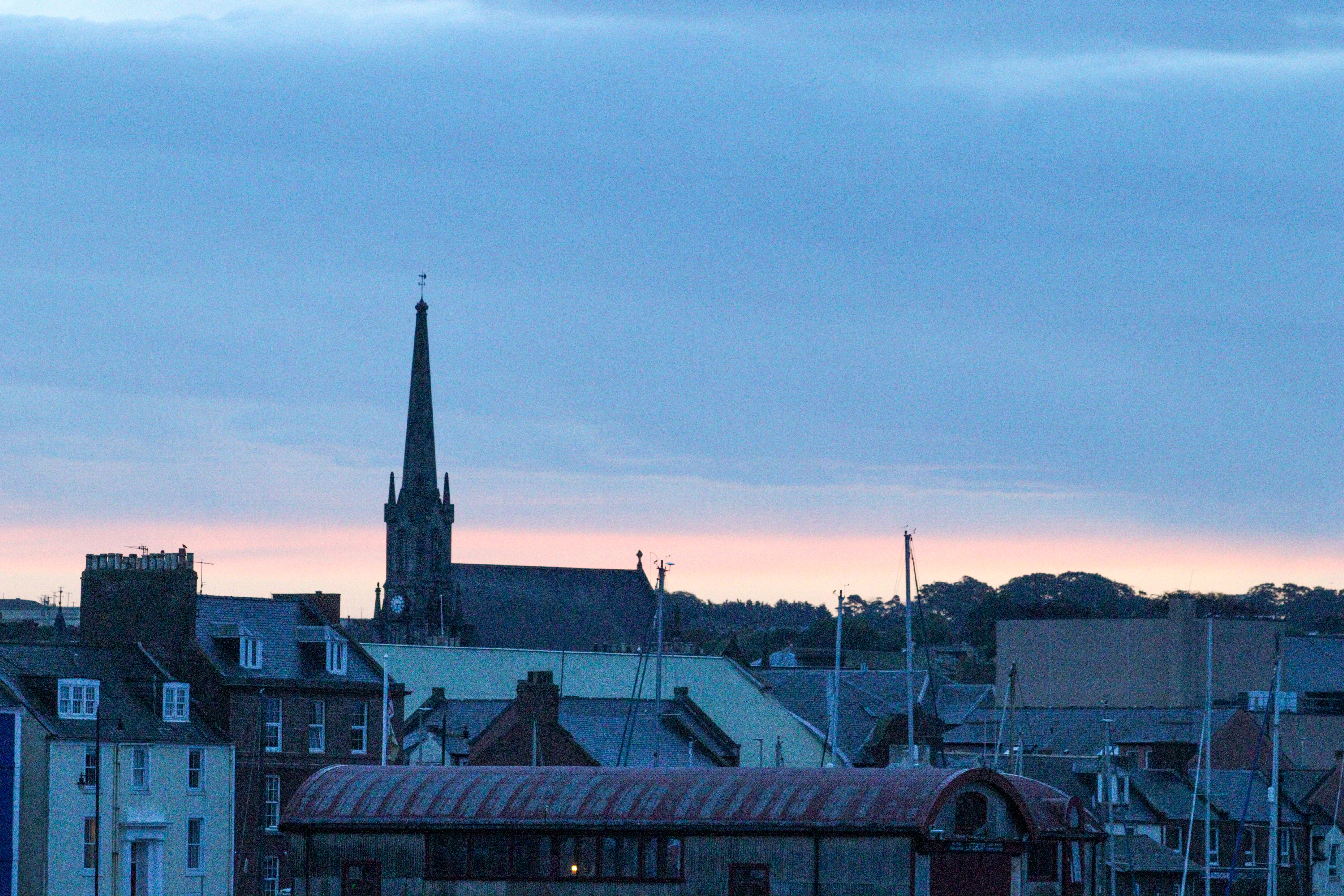 A church on a hill with ship masts below and a slightly red sunrise sky.