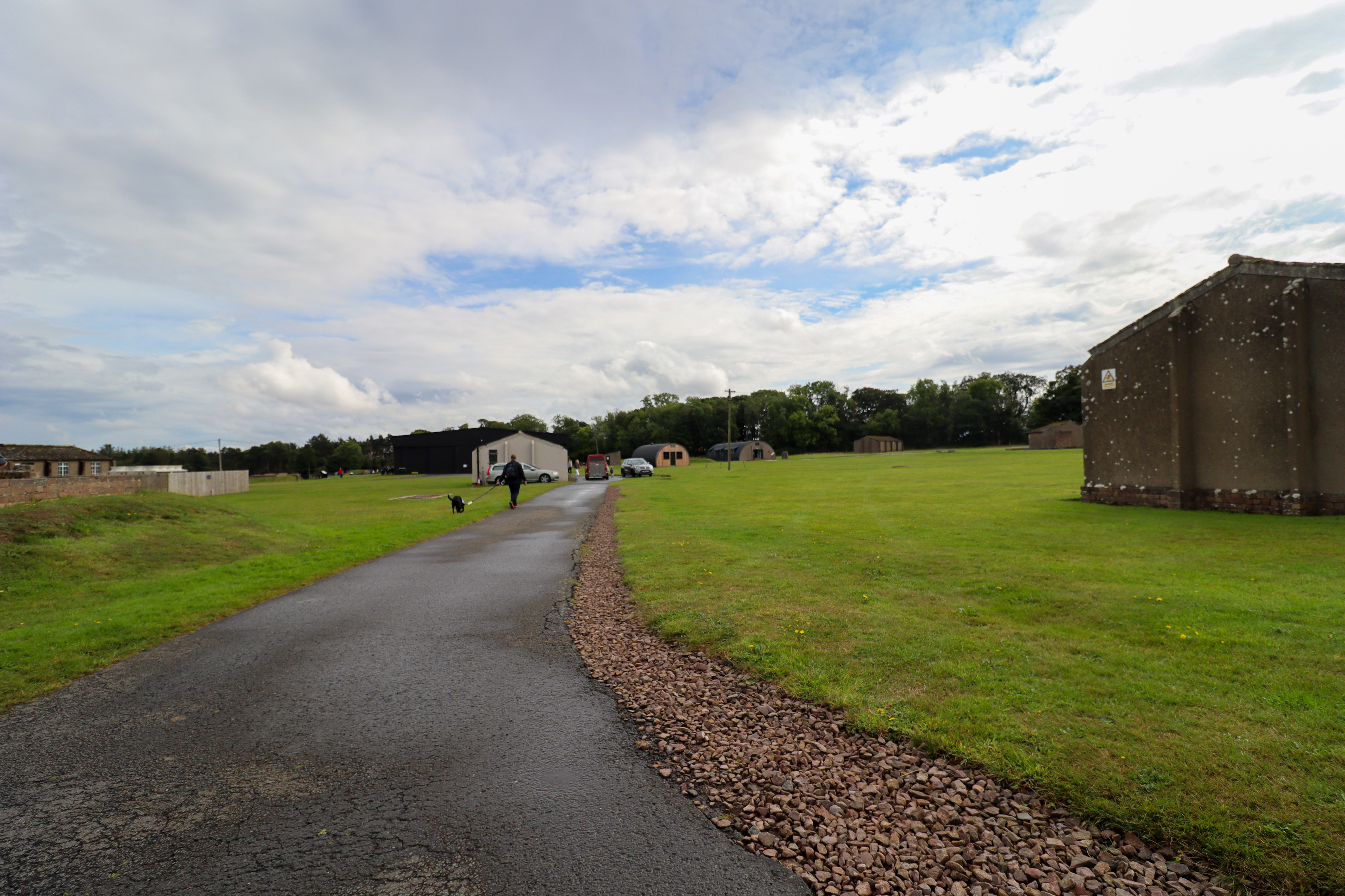 Large site with buildings dotted around and a man walking a black dog on the grass ahead