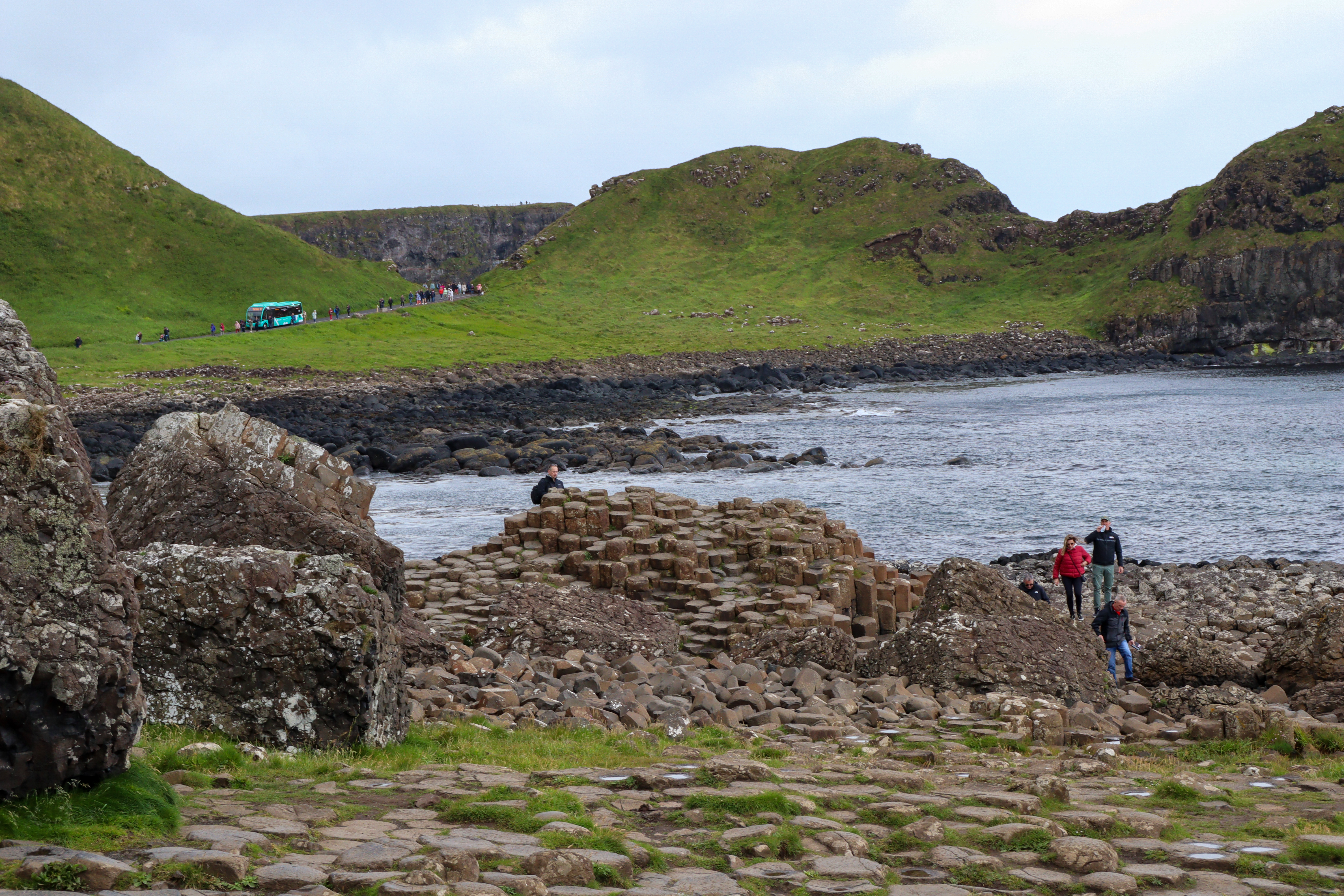 People climbing over the causeway stones, with the road in the background and a bus driving along it.