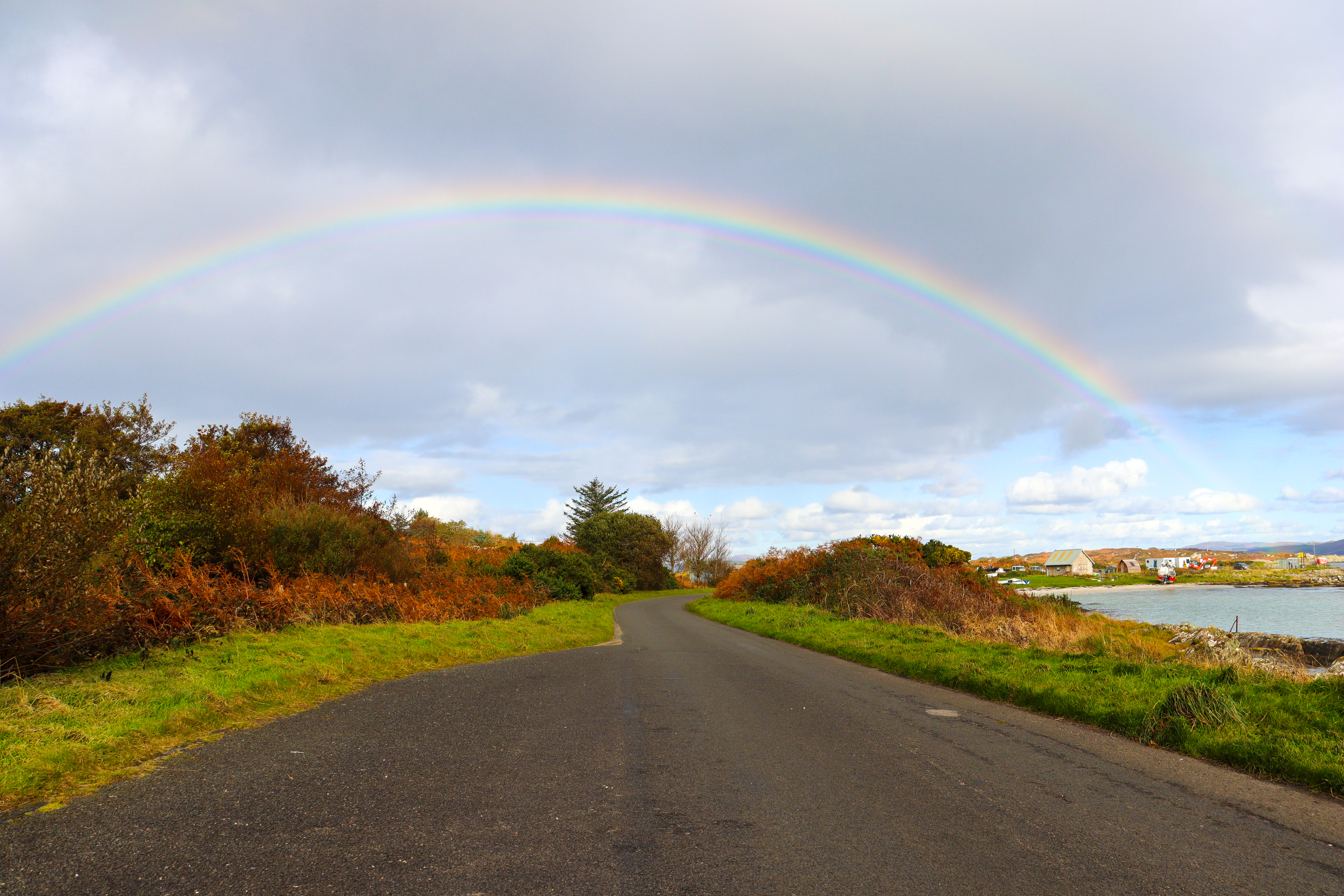 Road with sea to the right and a full rainbow covering them both.