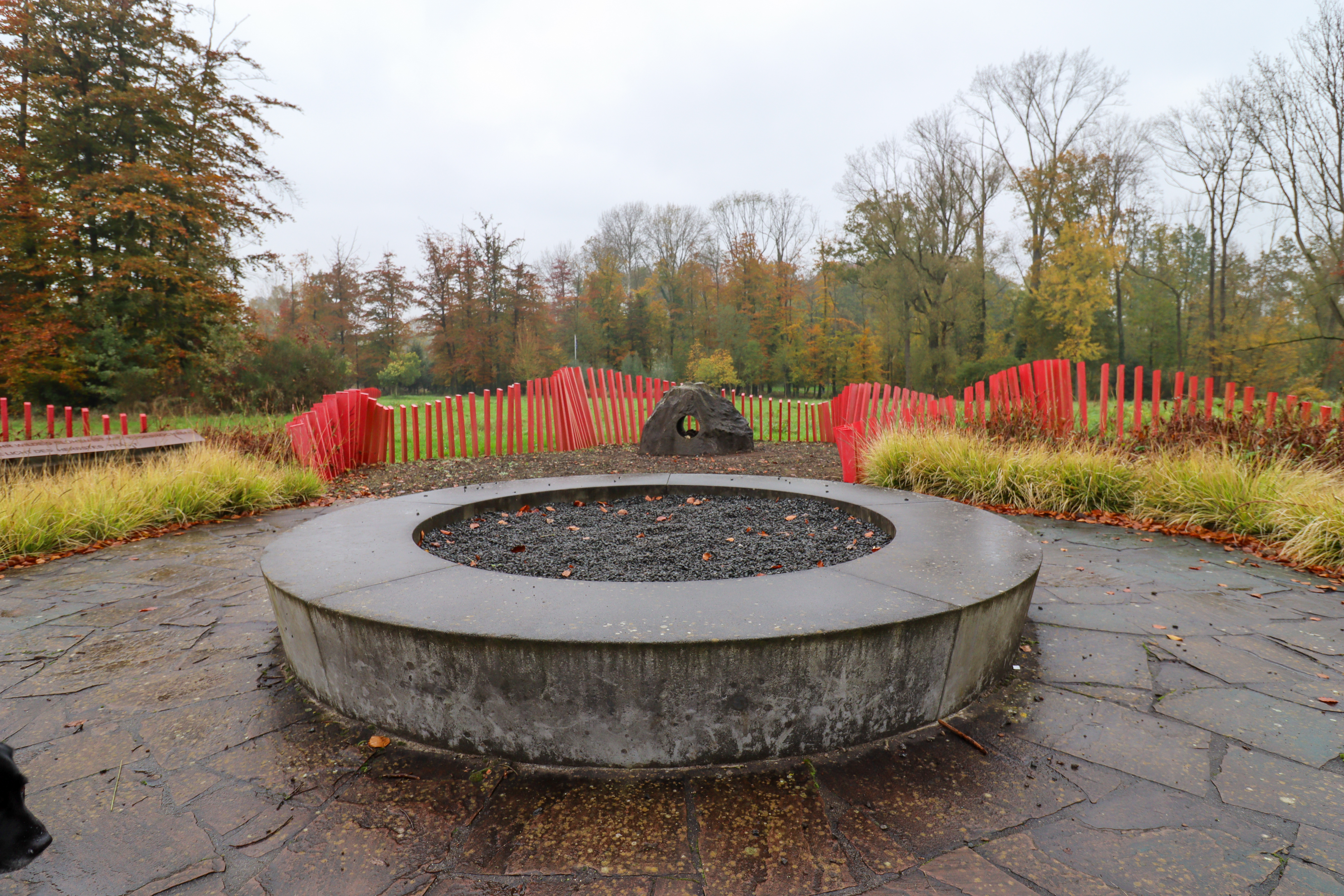 Garden with circular raised bed in the middle and a large stone with a hole through the middle at the end