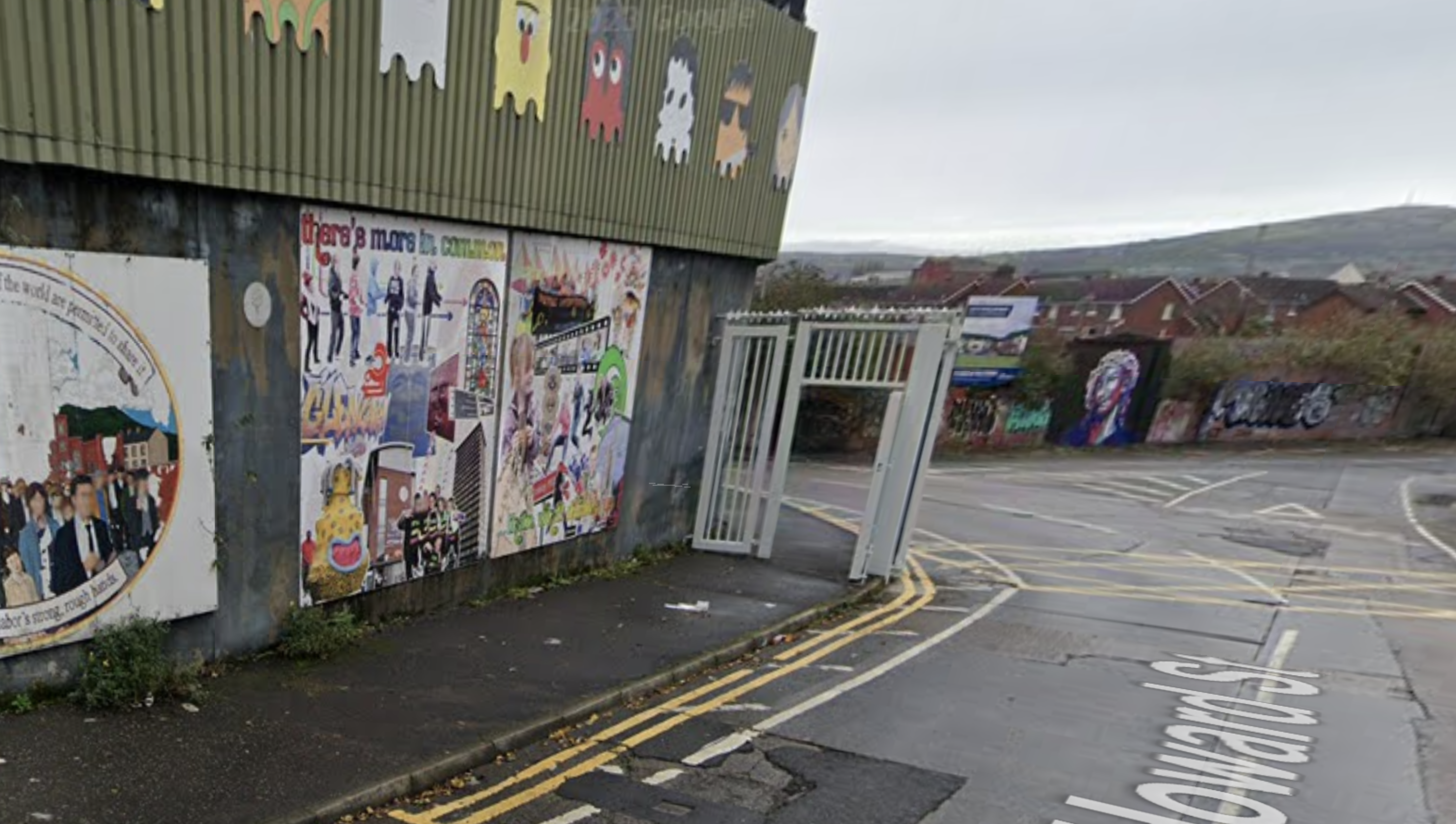Streetview showing a high wall covered in murals and graffiti, with an iron security gate with barbed wire on top.