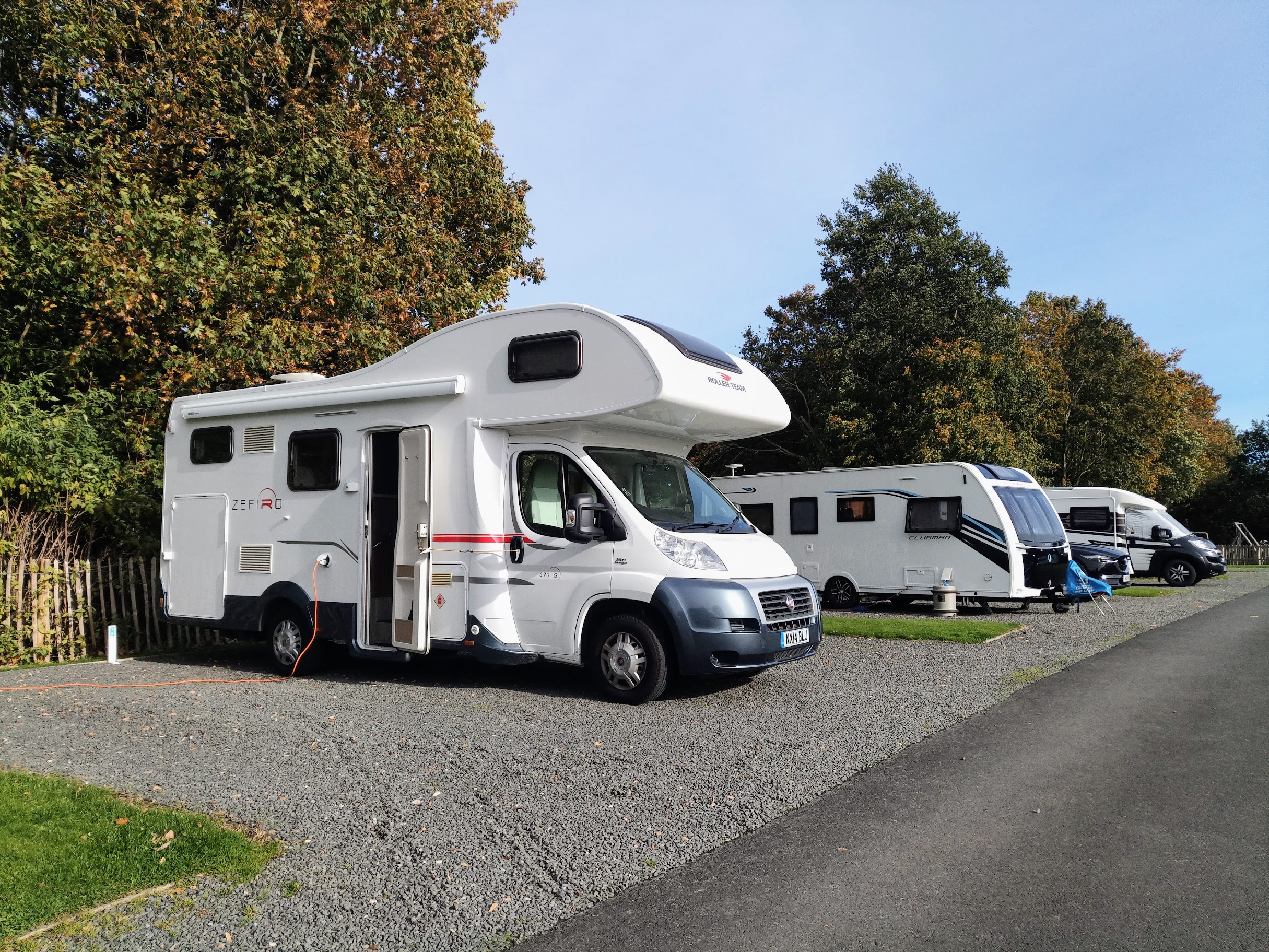 Motorhome pitched up on gravel with electric cable plugged in and caravans on adjacent pitches.