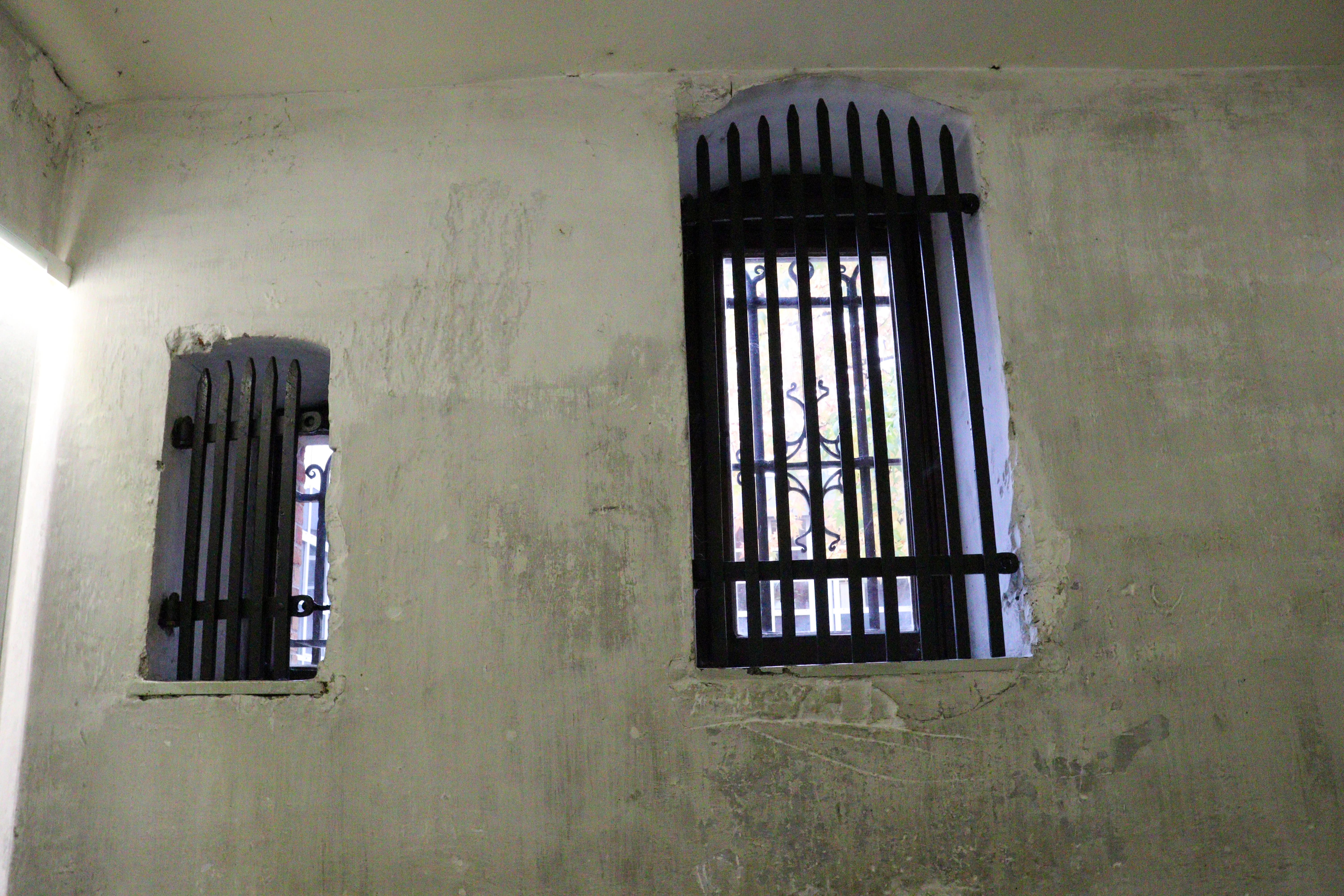 Dirty white cell wall with two tiny windows covered with black bars