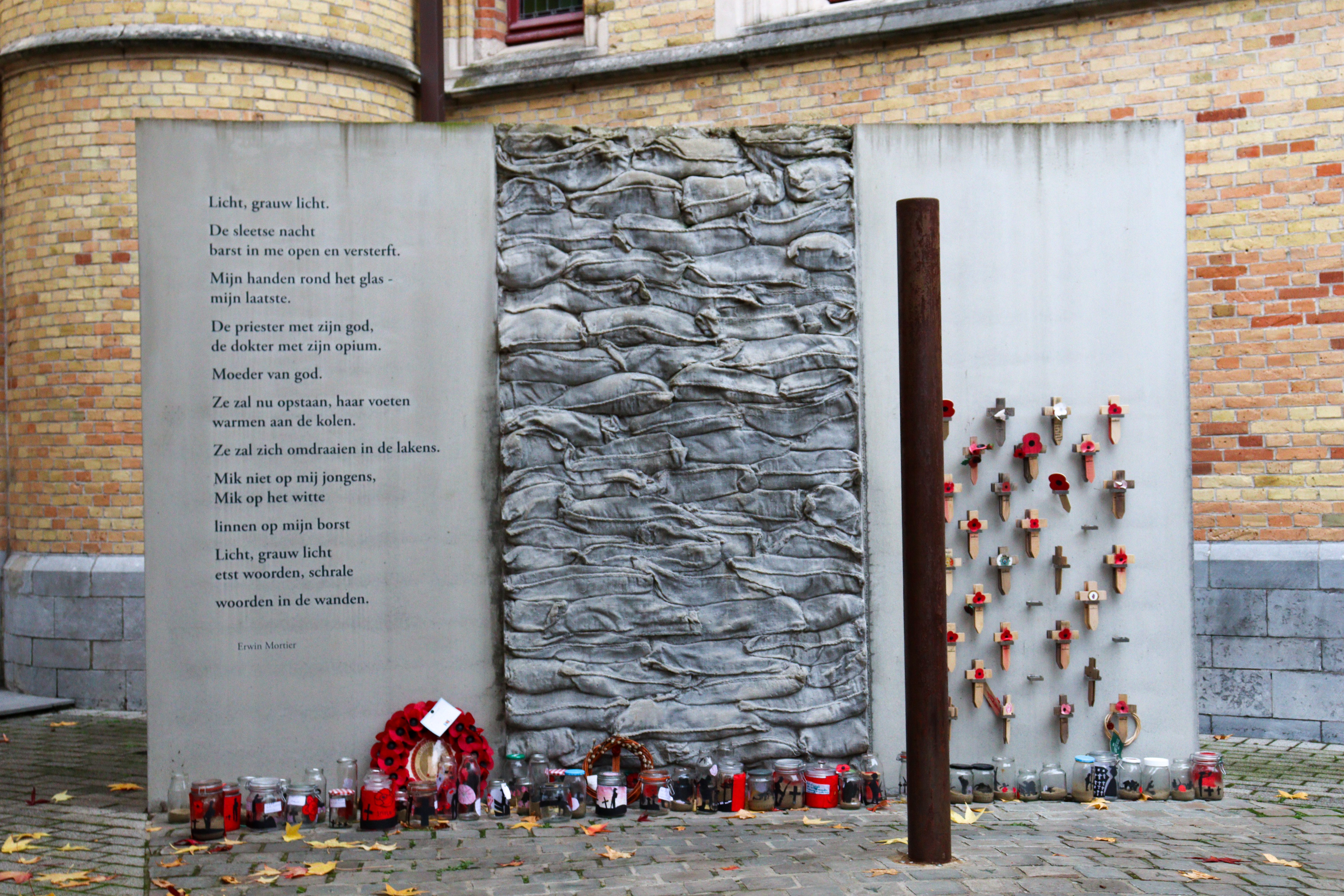 Rusty post with commemorative wall behind, with poppies and little wooden crosses