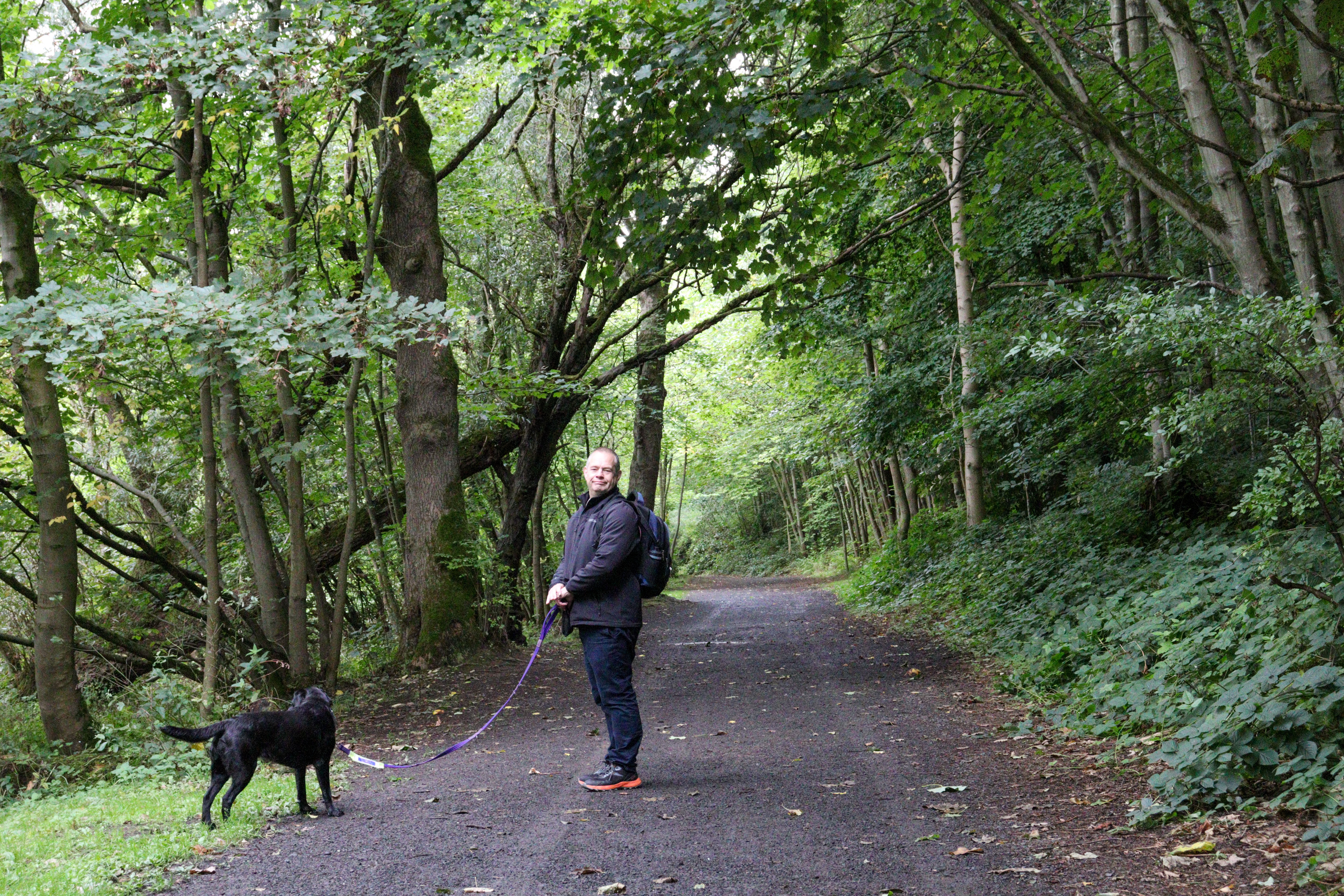 Man and black dog standing on a forest path on a slight hill.