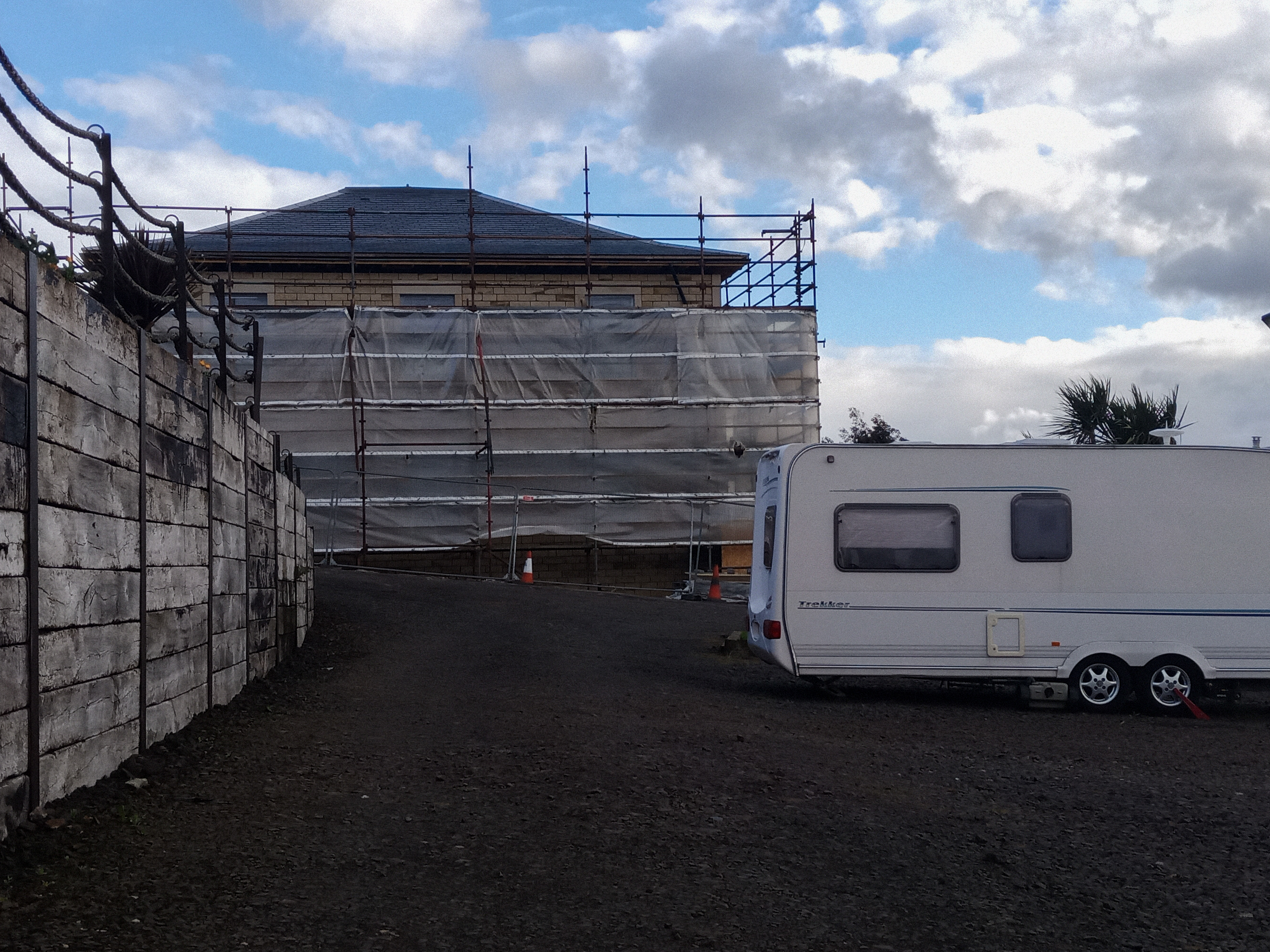Caravan site with high wooden wall on one side and building with scaffolding ahead
