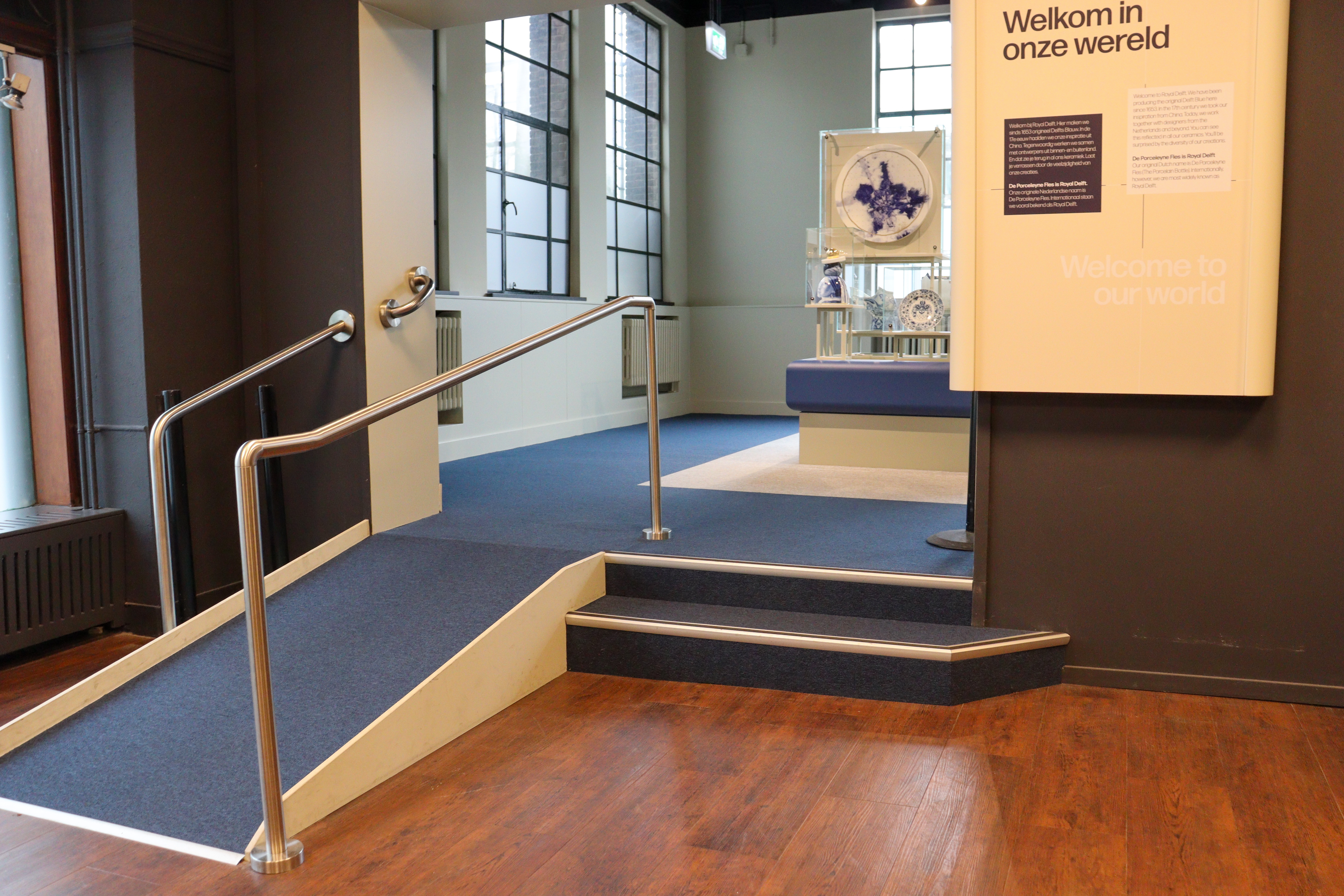 Entrance to museum with two steps and a fairly steep ramp with carpet on it