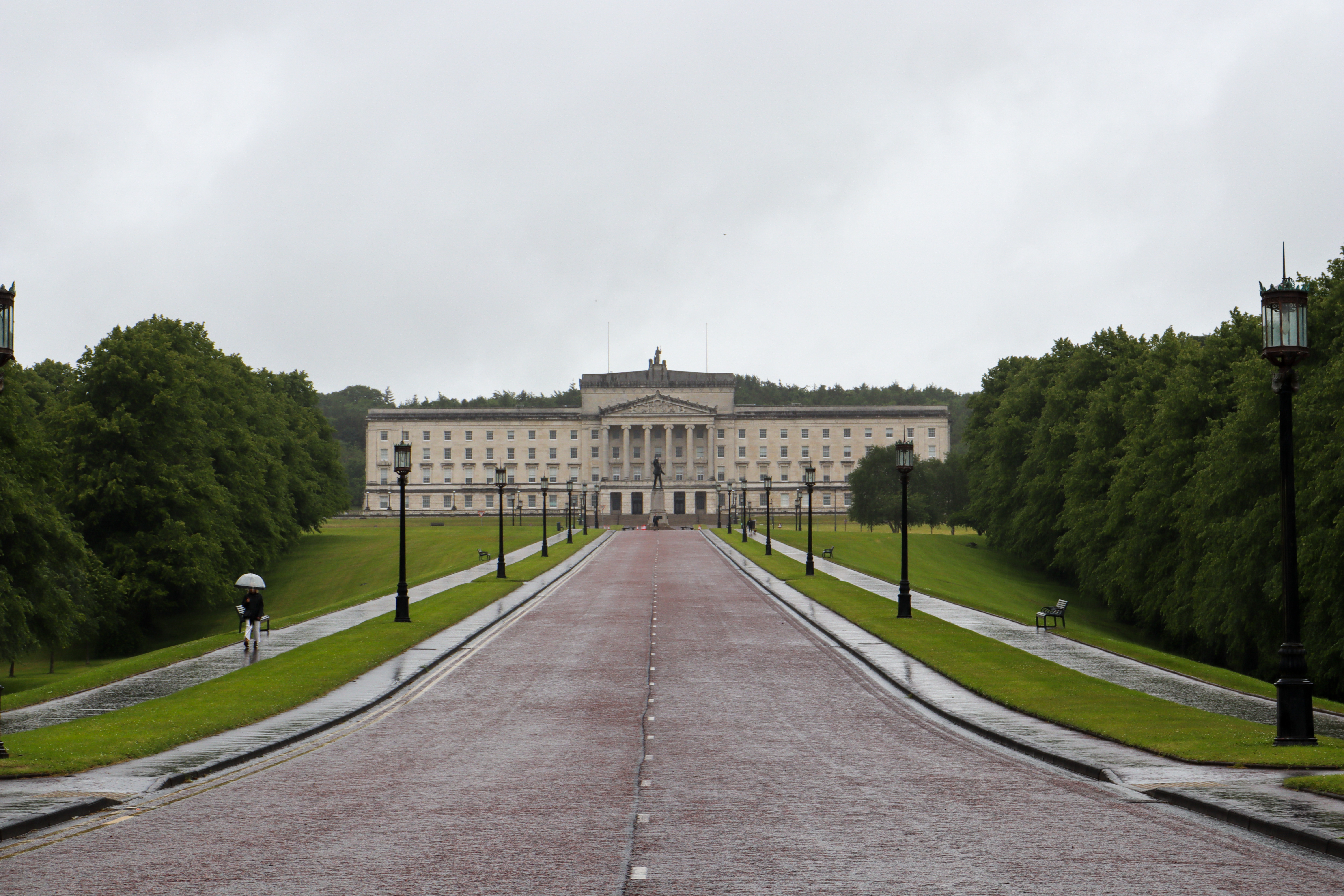 Tree lined road going uphill to a large white building. The whole image is perfectly symmetrical.