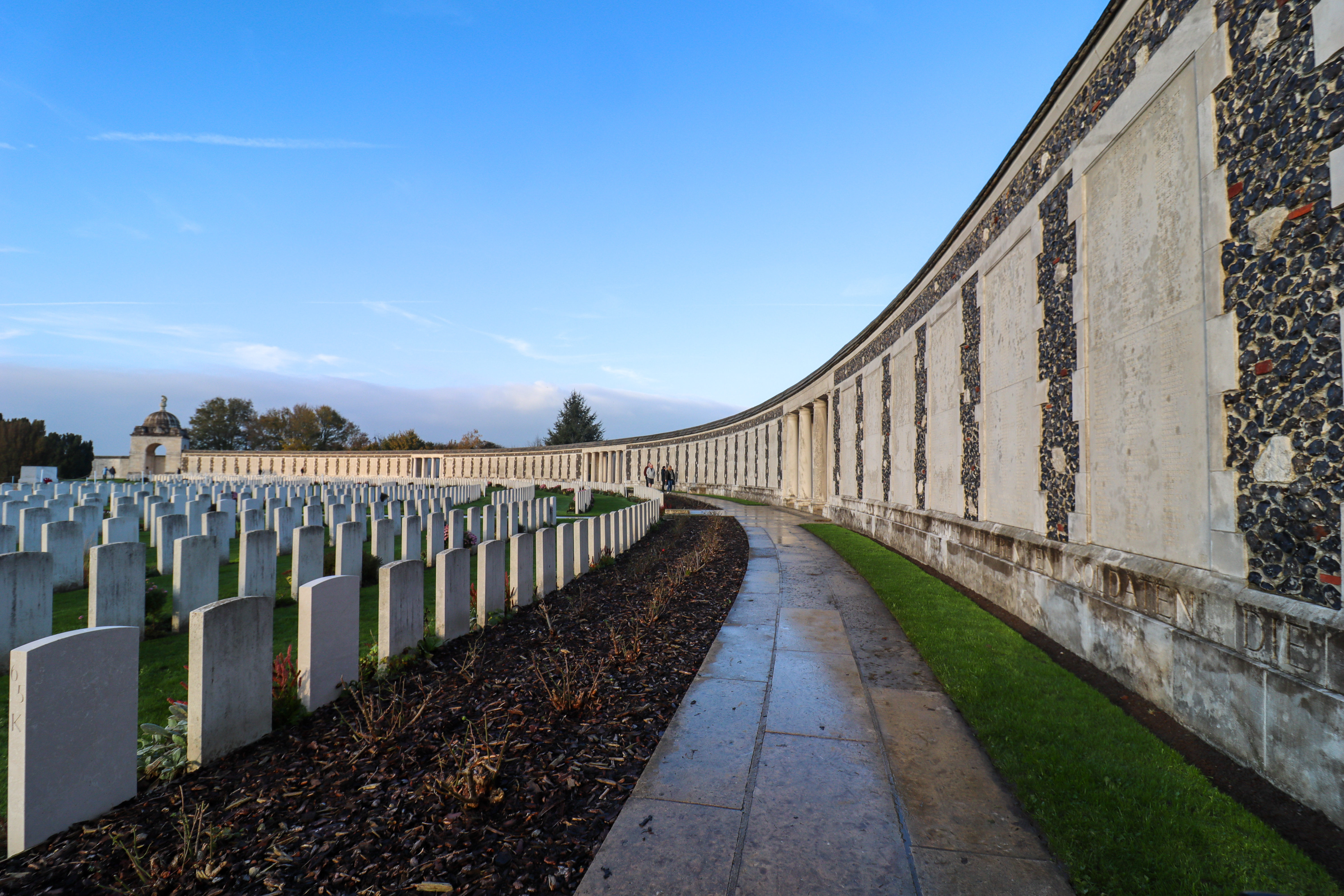 Path curving round to the left with a wall on the right covered with plaques and graves on the left