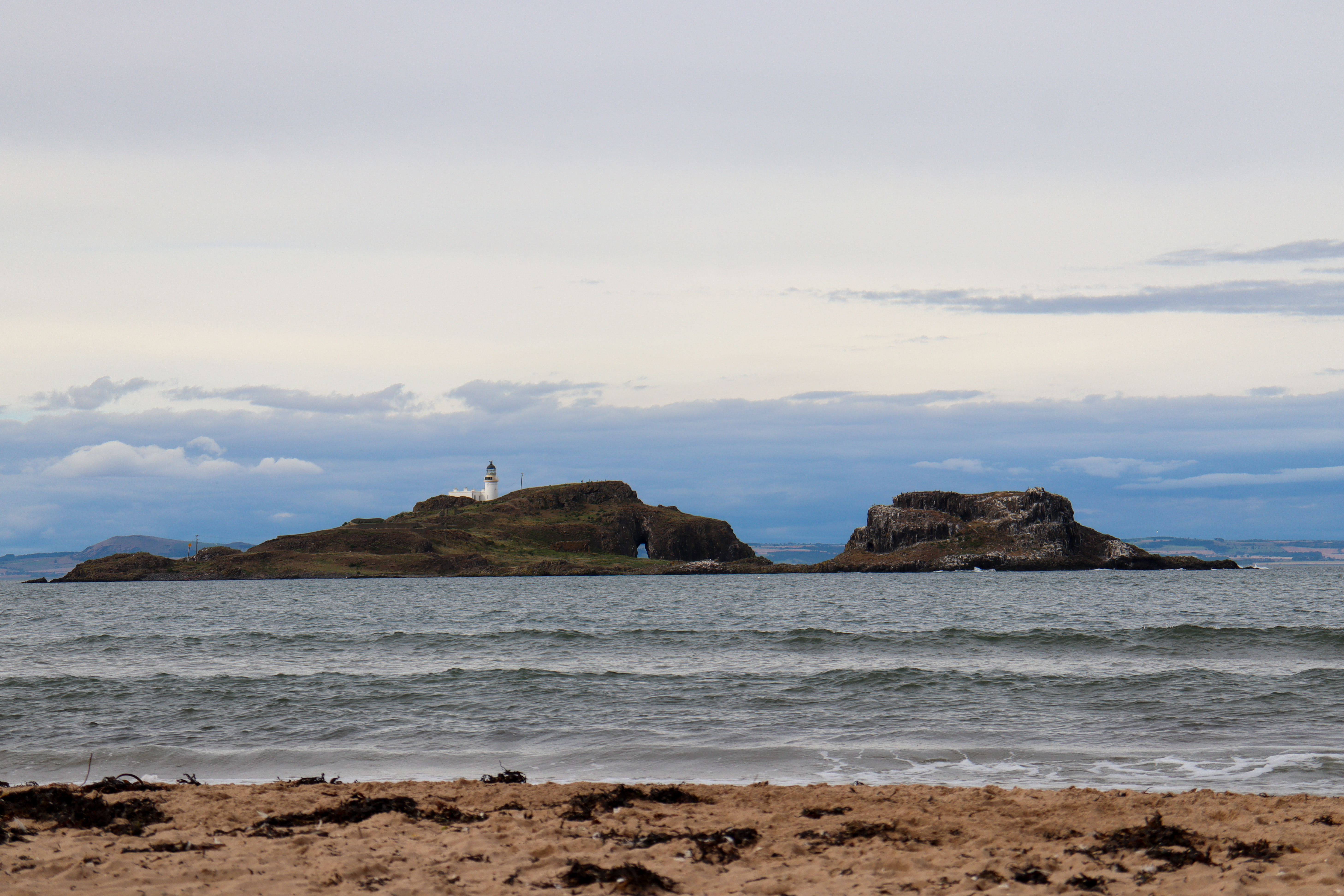 Small island which looks to have two halves to it. On the left half is a lighthouse.
