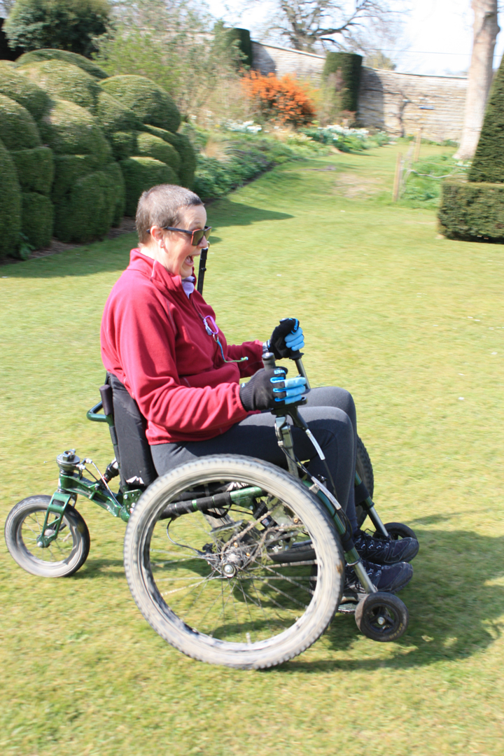 Nicki in an off-road wheelchair with hand levers, rolling down a grassy bank.
